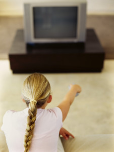 rear view of a girl pointing remote to a television